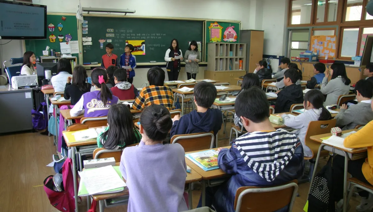 Sala de aula cheia vista do fundo, com alunos voltados para a lousa